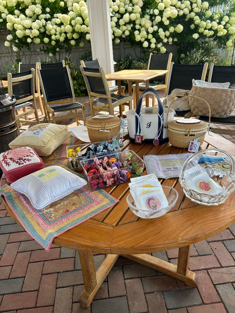 Pillows, baskets, threads, and canvases set out on a table under the hydrangeas